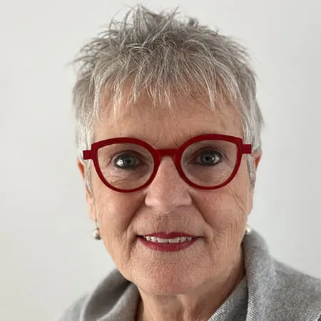 Présentation de l’auteure Ginette Plante | DistributionDPA Portrait of a smiling older woman with short gray hair and red round glasses against a light background.